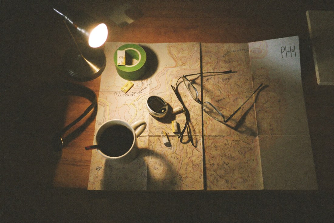 A topographic map, coffee, a headlamp, and gels spread across a kitchen table at night